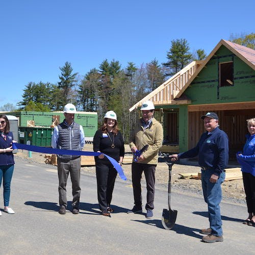 Six people in front of a framed home doing a ribbon cutting>